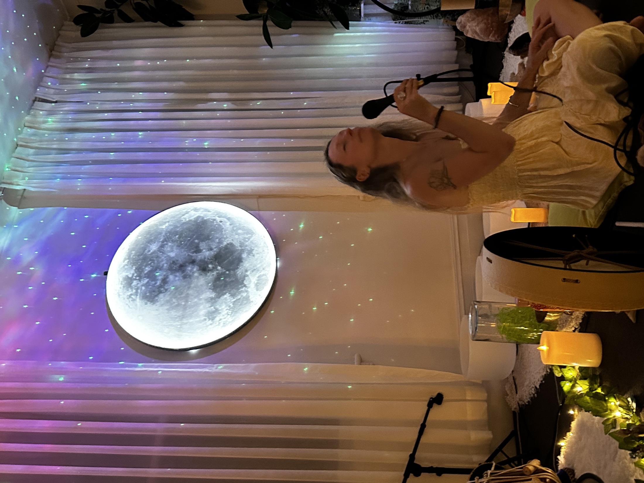 Giada Lovelight offering vocal healing beside the Mystic Wellness moon wall