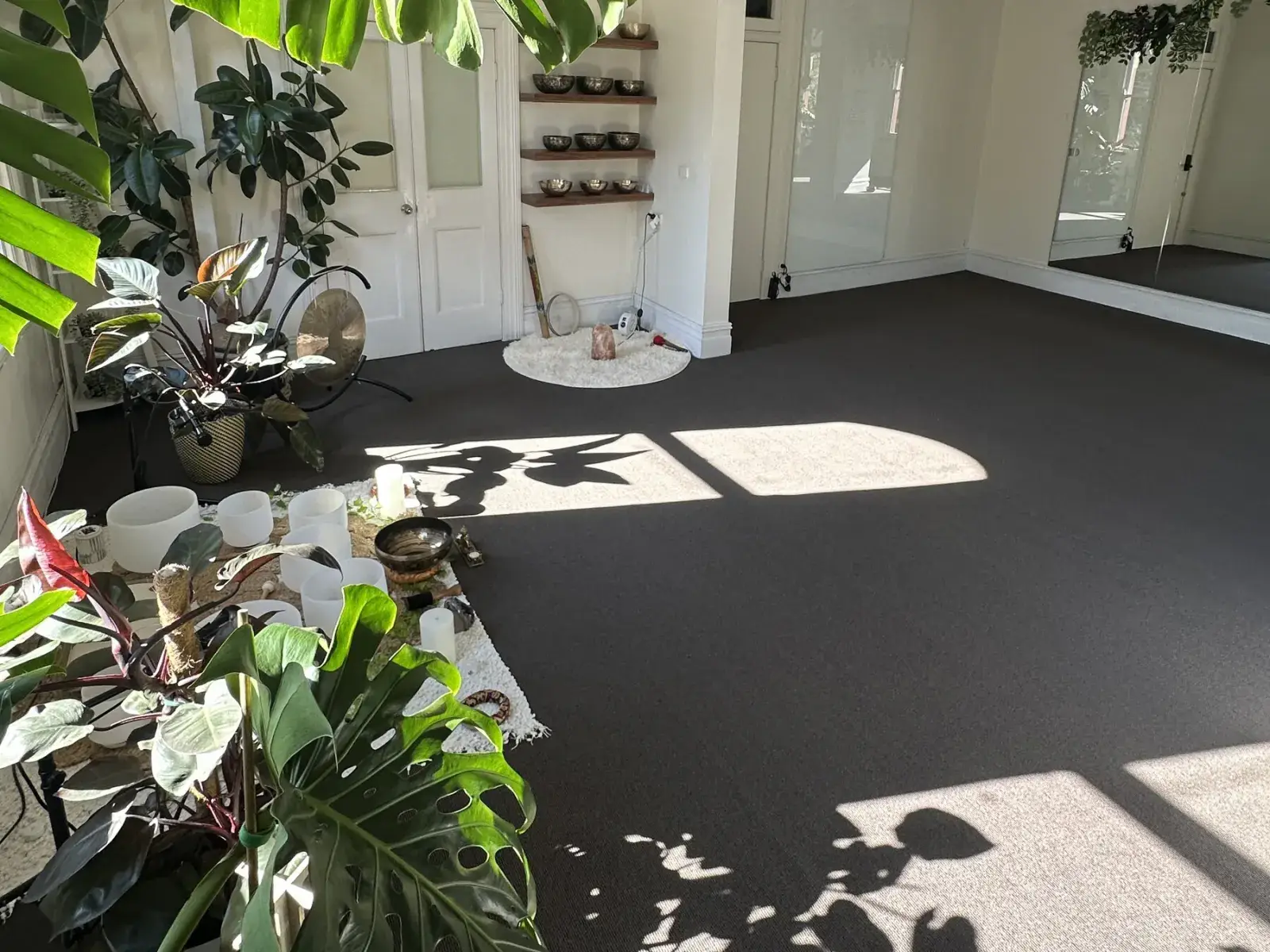 Sunlit Mystic Wellness studio rental space with plants, mirrors, bowls, and open floor in Petersham