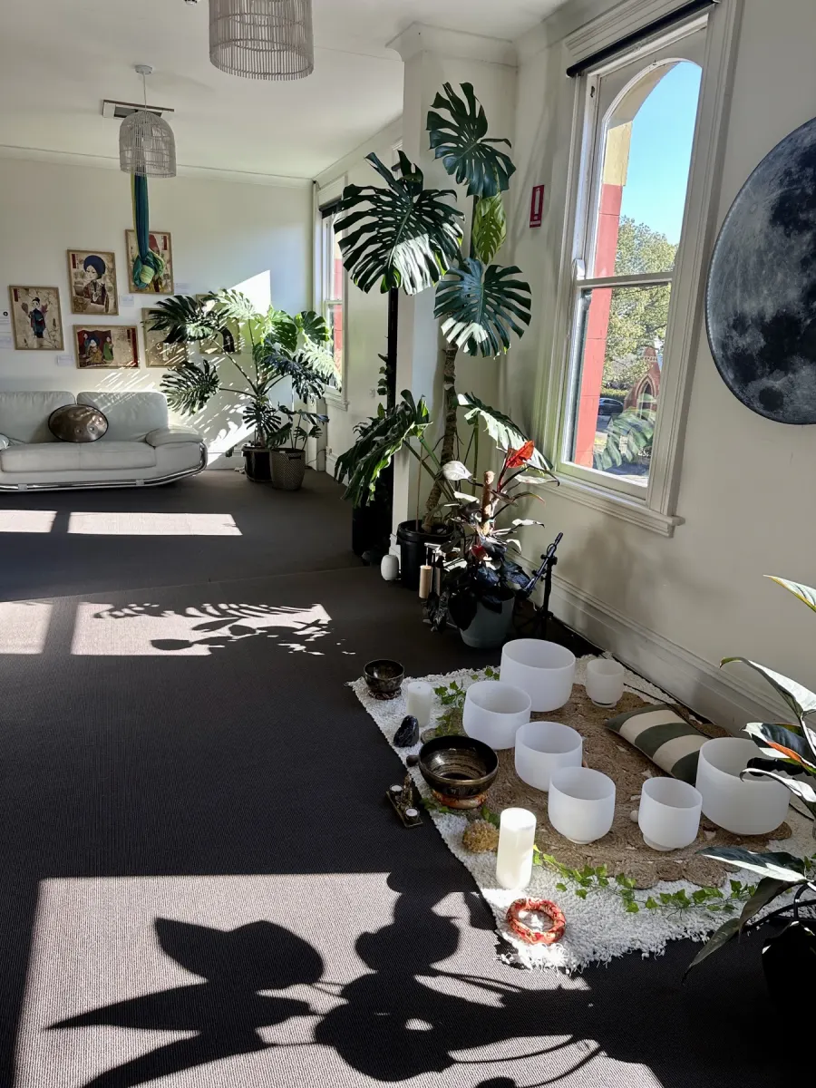 Sunlit Mystic Wellness studio rental space with moon wall, plants, windows, and singing bowls in Petersham
